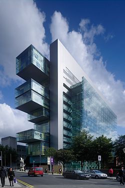 External view showing the glazed volume of the atrium projecting from the metal-clad spine wall.