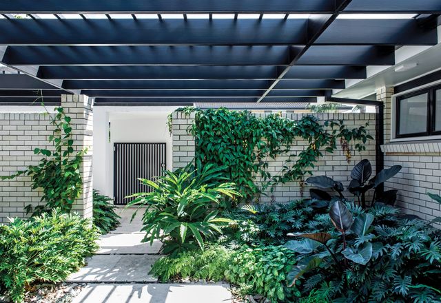 The entry courtyard is a mix of shades of grey and green that highlights various foliage textures, with a ground layer of travertine pavers over sandstone river pebbles.