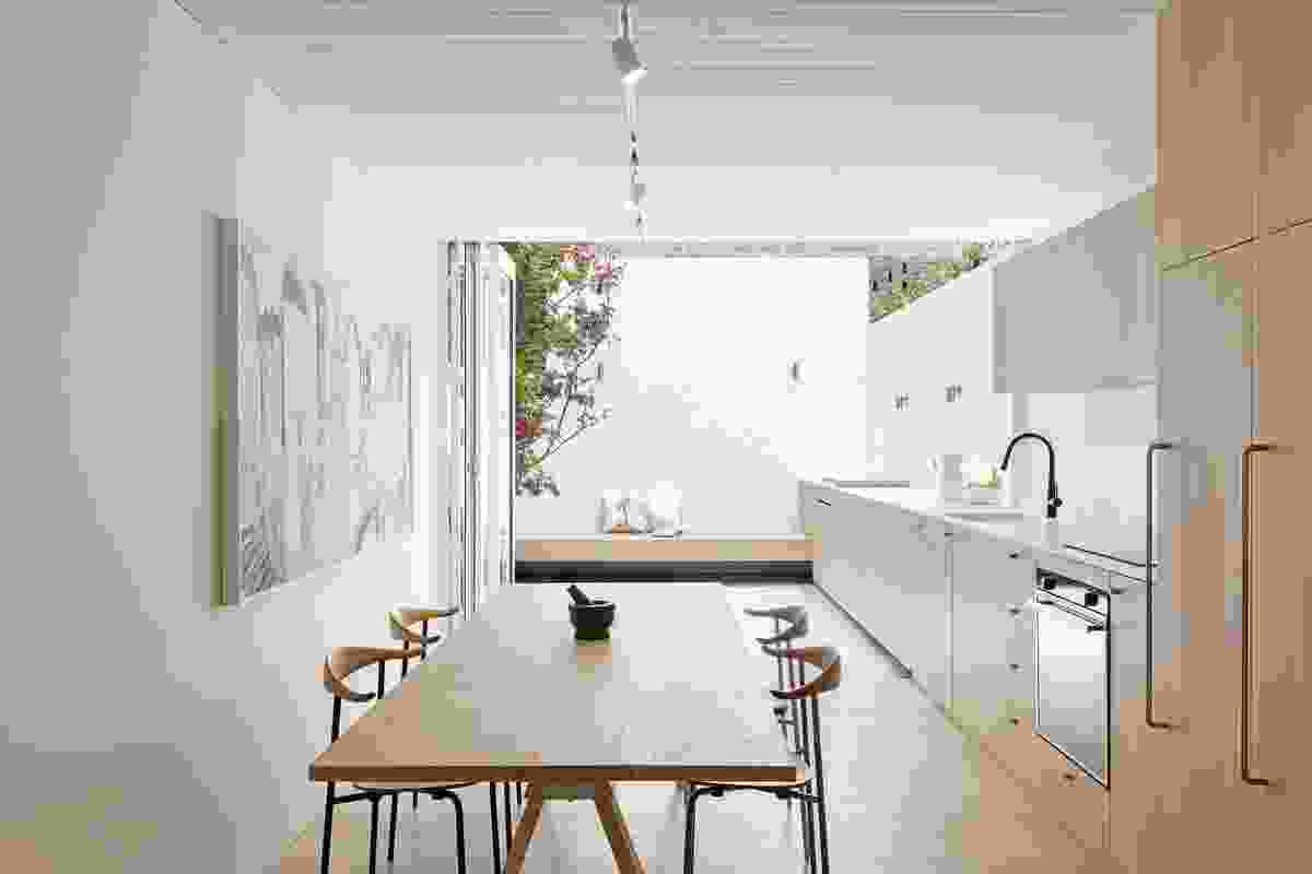 The kitchen extends seamlessly through bifold doors to a sunlit courtyard. Artwork: Mark Hanman.